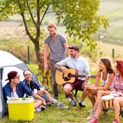 Group of young men and women having fun and playing guitar in nature