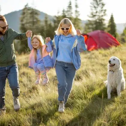 Young caucasian couple with little girl and dog have fun spending leisure time together while travel with tent in the mountains. Happy family summer vacation at campsite